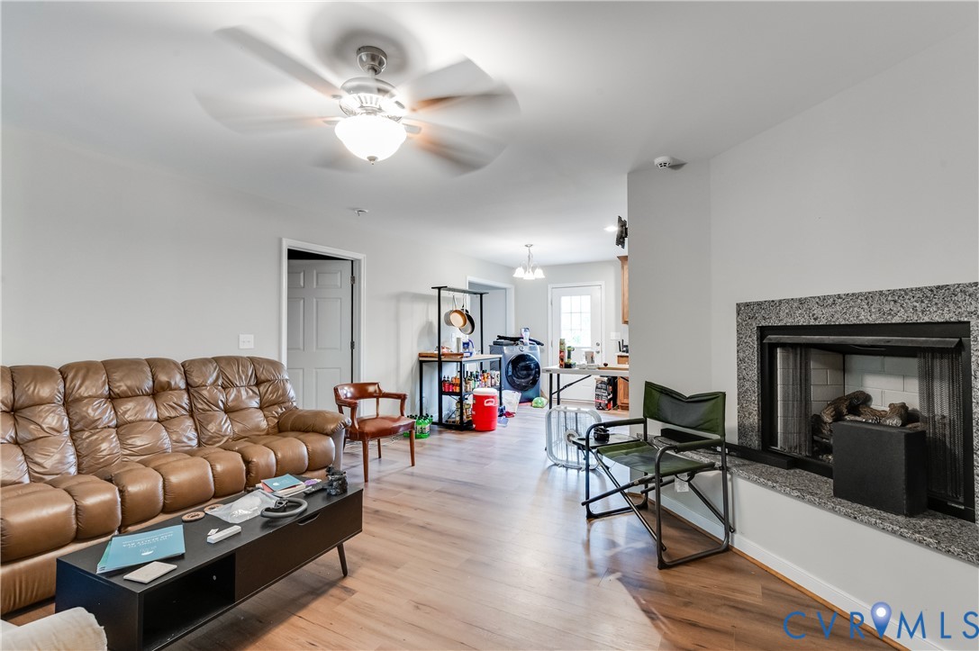 Living room featuring wood-finish flooring, a ceiling fan with integrated lighting, a fireplace with a granite surround, and a clear doorway Living room featuring wood-finish flooring, a ceiling fan with integrated lighting, a fireplace with a granite surround, and a clear doorway