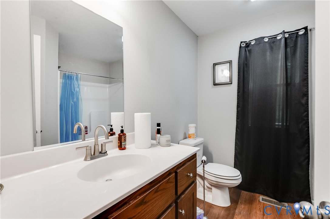 Bathroom featuring a wood-finish vanity with a white countertop and integrated sink, brushed nickel faucet, and wood-finish flooring Bathroom featuring a wood-finish vanity with a white countertop and integrated sink, brushed nickel faucet, and wood-finish flooring