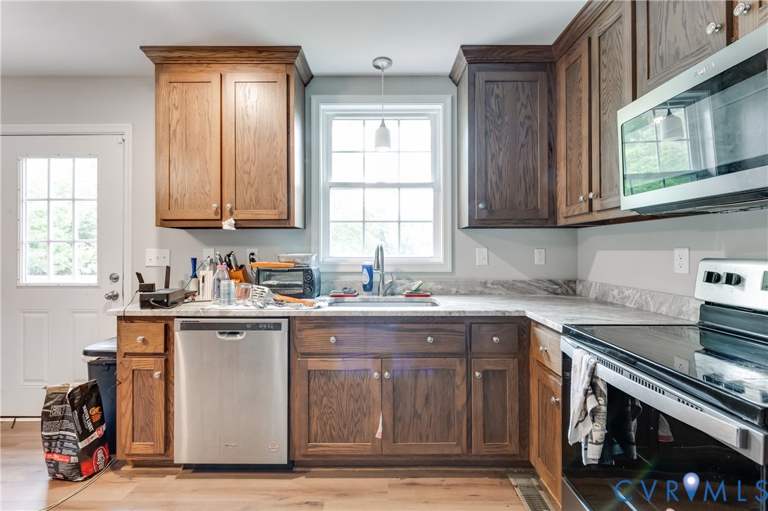 Kitchen featuring wood-finish cabinetry, light-toned countertops, stainless steel appliances, a window above the sink, and wood-finish flooring