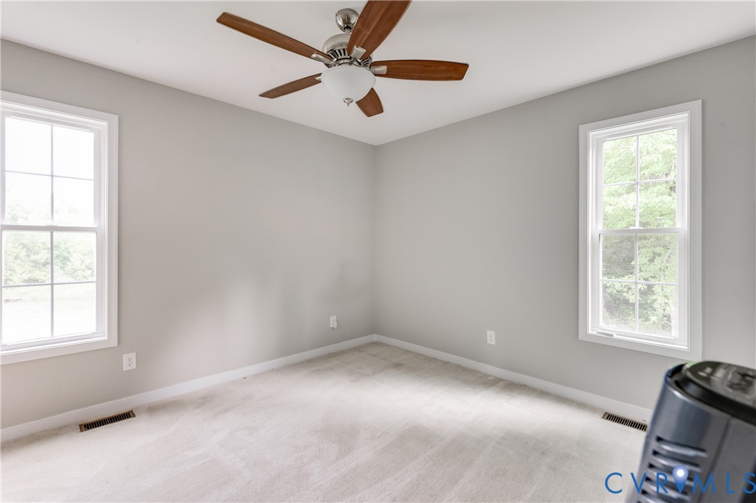 Carpeted room with light grey walls, two windows, and a ceiling fan with light fixture Carpeted room with light grey walls, two windows, and a ceiling fan with light fixture