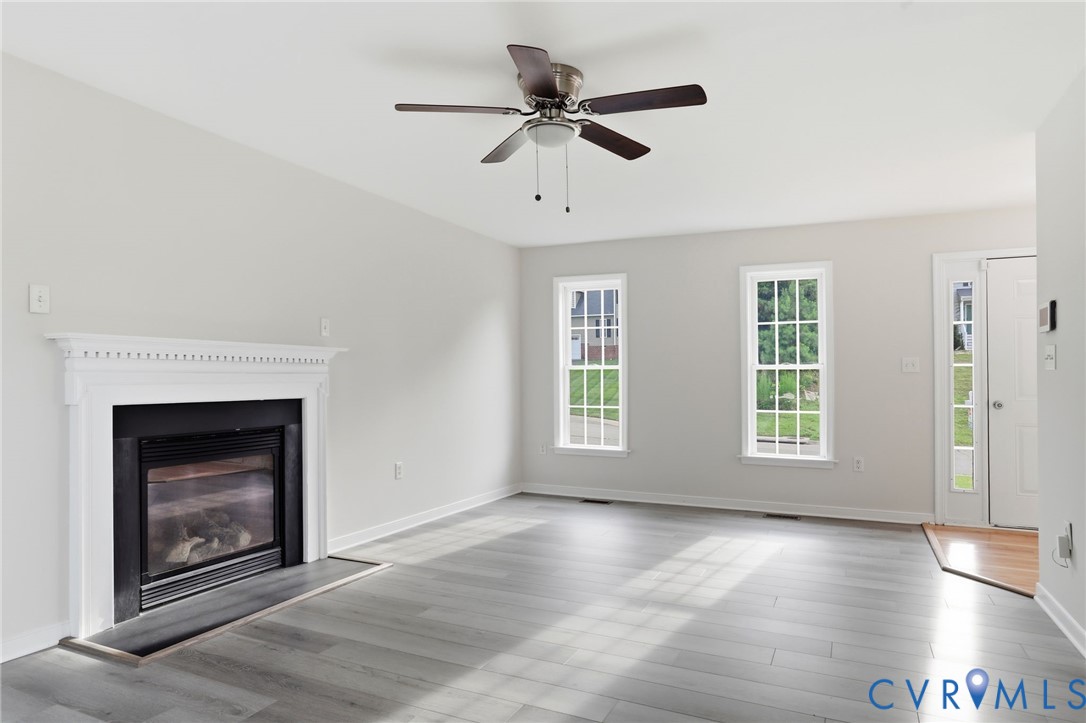 Spacious interior featuring a white mantel fireplace with black insert, wood-finish flooring, and multiple windows