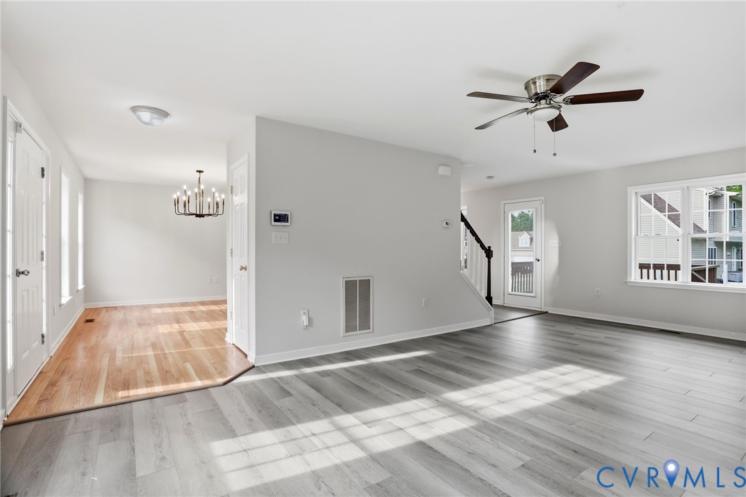 Spacious living area featuring light gray wood-finish flooring, a contemporary ceiling fan, and large windows
