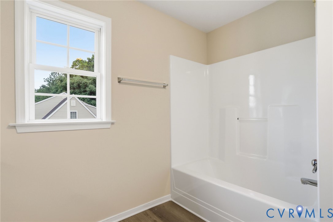 Bright bathroom featuring a single-hung window with grilles, a white fiberglass tub/shower combination, polished chrome fixtures, and wood-finish flooring
