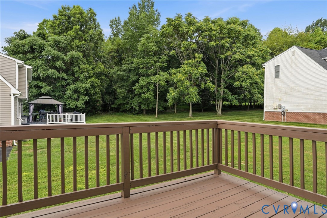 Expansive wooden deck with coordinating railings, overlooking a grassy yard bordered by mature trees