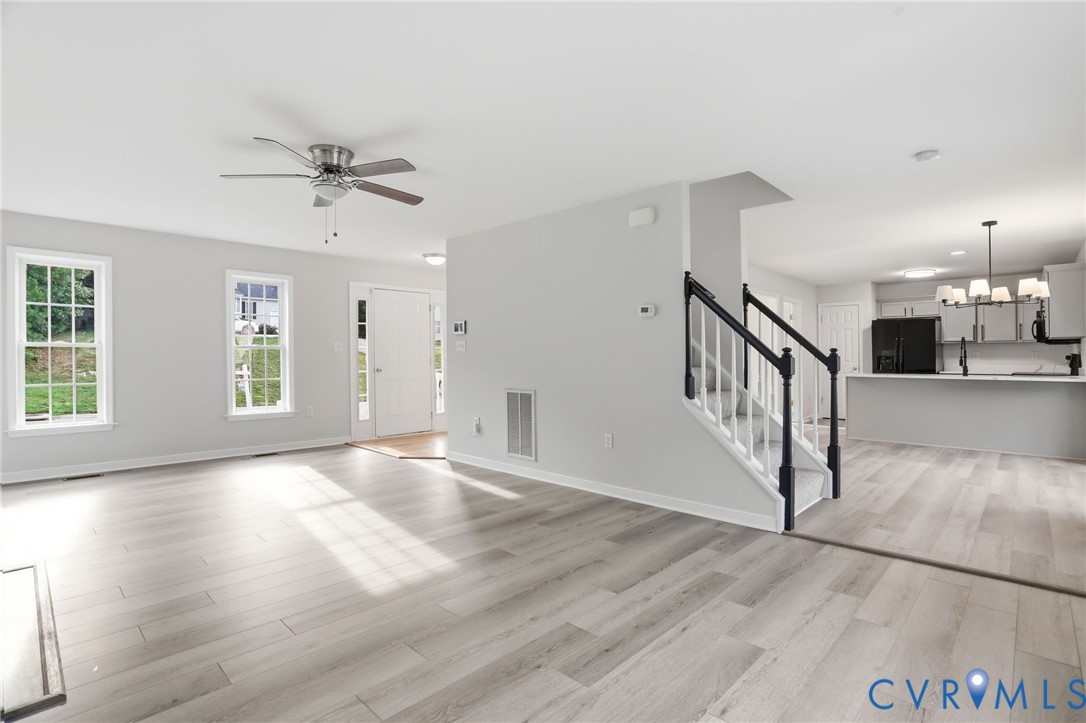 Spacious living area featuring light wood-finish flooring, a ceiling fan, and multiple windows