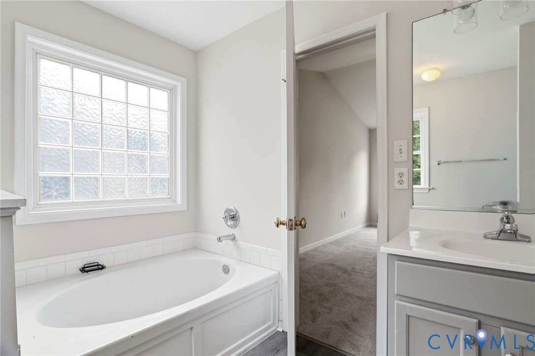 Soaking tub with a large glass block window, chrome fixtures, and a white tile surround