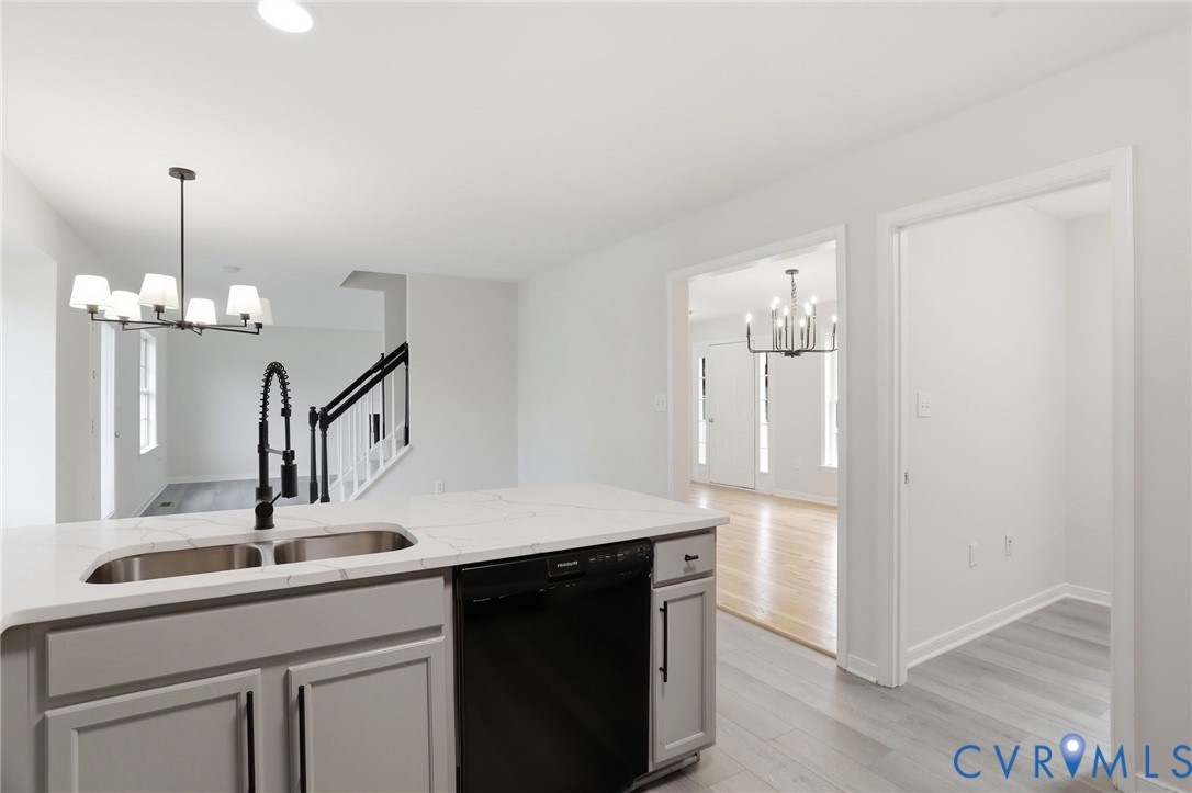 Kitchen island featuring a dual-basin stainless steel sink, black gooseneck faucet, light-toned countertop, and light gray cabinetry