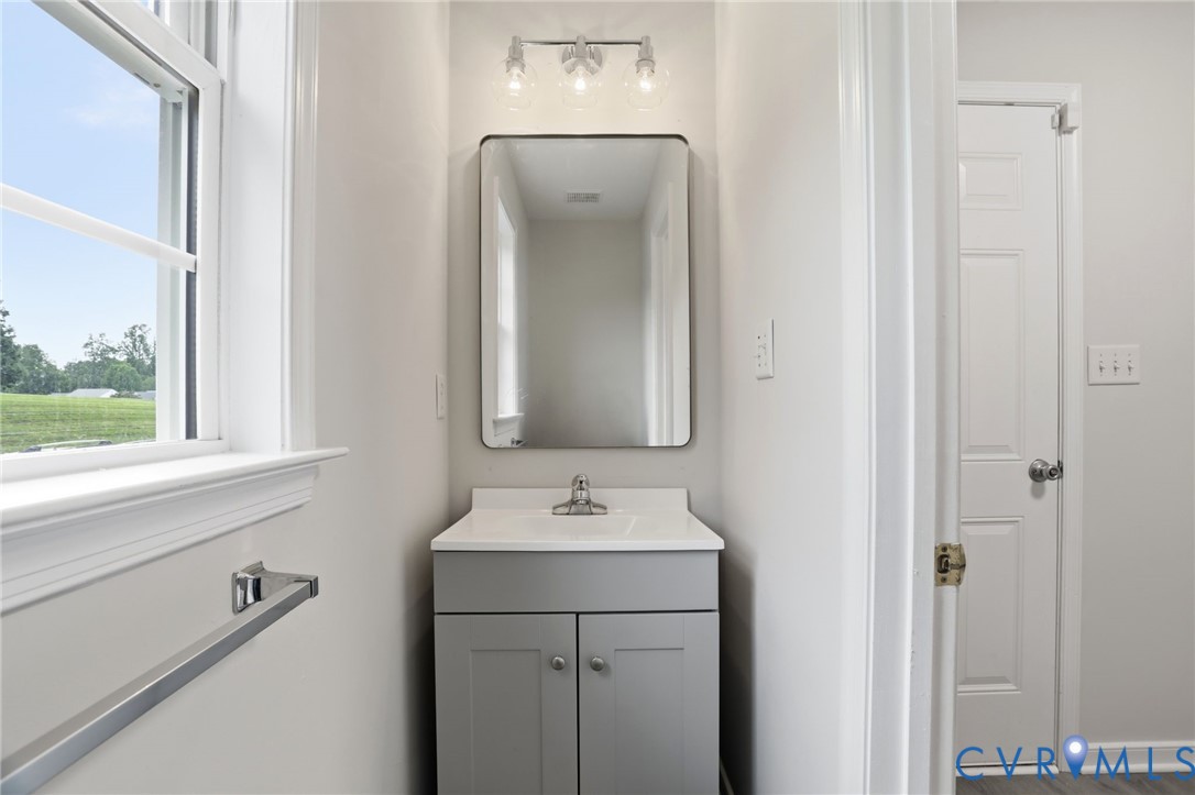 Bathroom vanity featuring a light gray cabinet base with brushed nickel hardware, a white countertop, and a rectangular mirror with integrated lighting