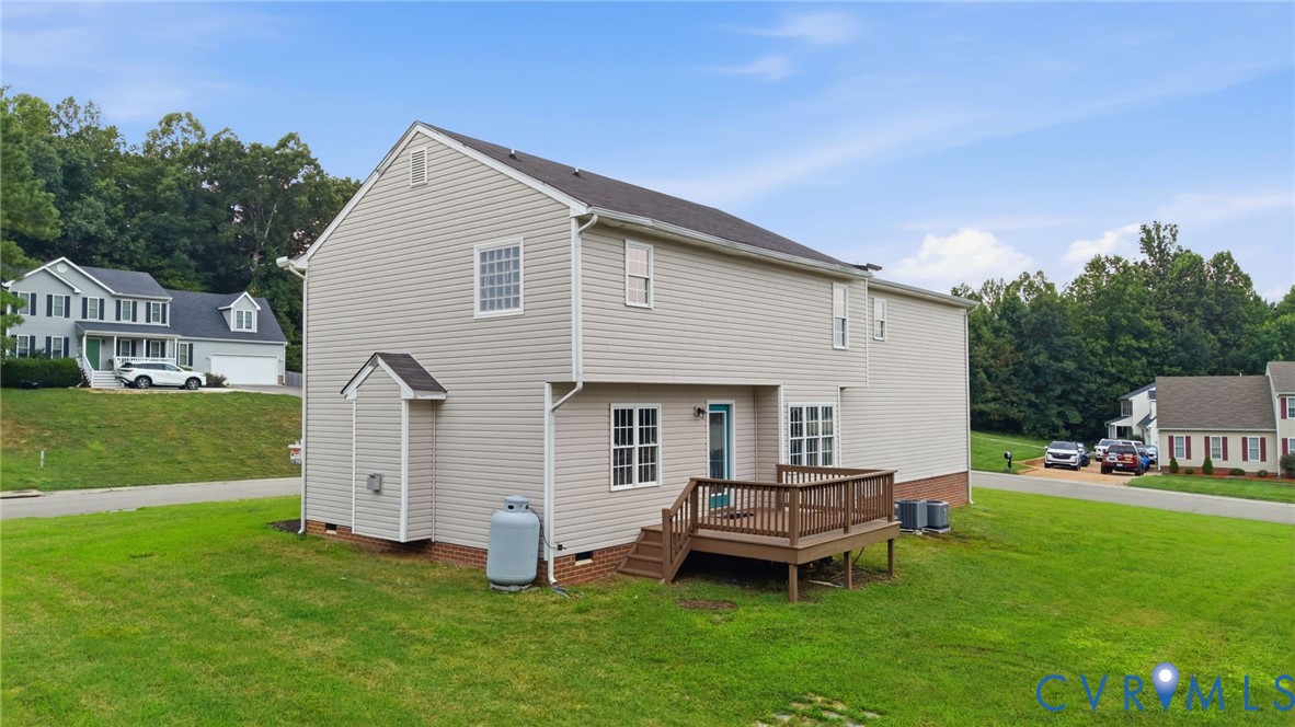 Rear exterior featuring a wooden deck, light-colored siding, multiple windows, and a manicured lawn