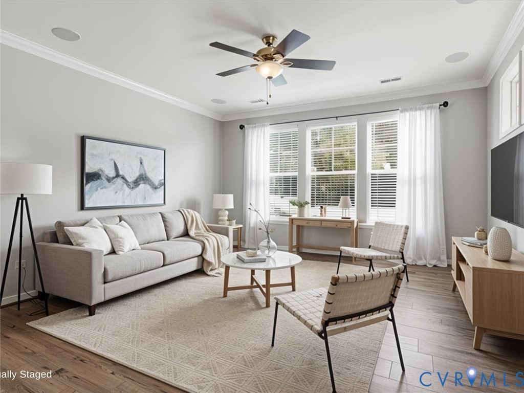 The sun-filled living room features luxury vinyl plank flooring, built-in surround sound speakers, elegant crown molding, and a ceiling fan, creating a warm and inviting space for everyday living or entertaining The sun-filled living room features luxury vinyl plank flooring, built-in surround sound speakers, elegant crown molding, and a ceiling fan, creating a warm and inviting space for everyday living or entertaining