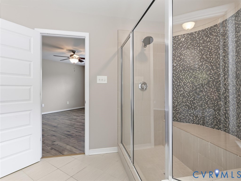 The spa-inspired primary bathroom boasts an oversized tiled walk-in shower with sleek glass enclosure, a built-in bench with striking mosaic tile accents, and neutral designer finishes for a timeless, sophisticated look.