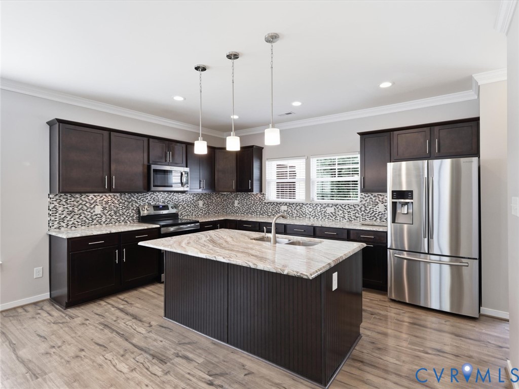 The chef-inspired kitchen showcases rich espresso cabinetry, granite countertops, a stylish tile backsplash, stainless steel appliances, luxury vinyl plank flooring, and an oversized island with bar seating, all beautifully illuminated by pendant and recessed lighting.