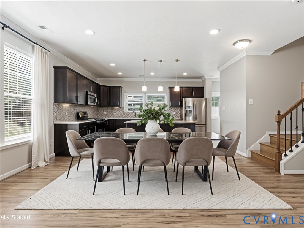 The spacious dining area seamlessly connects to the kitchen, creating an ideal setting for everyday meals or entertaining. Highlighted by luxury vinyl plank flooring, elegant crown molding, and abundant natural light, it comfortably accommodates a large dining table while maintaining the home's open-concept design The spacious dining area seamlessly connects to the kitchen, creating an ideal setting for everyday meals or entertaining. Highlighted by luxury vinyl plank flooring, elegant crown molding, and abundant natural light, it comfortably accommodates a large dining table while maintaining the home's open-concept design