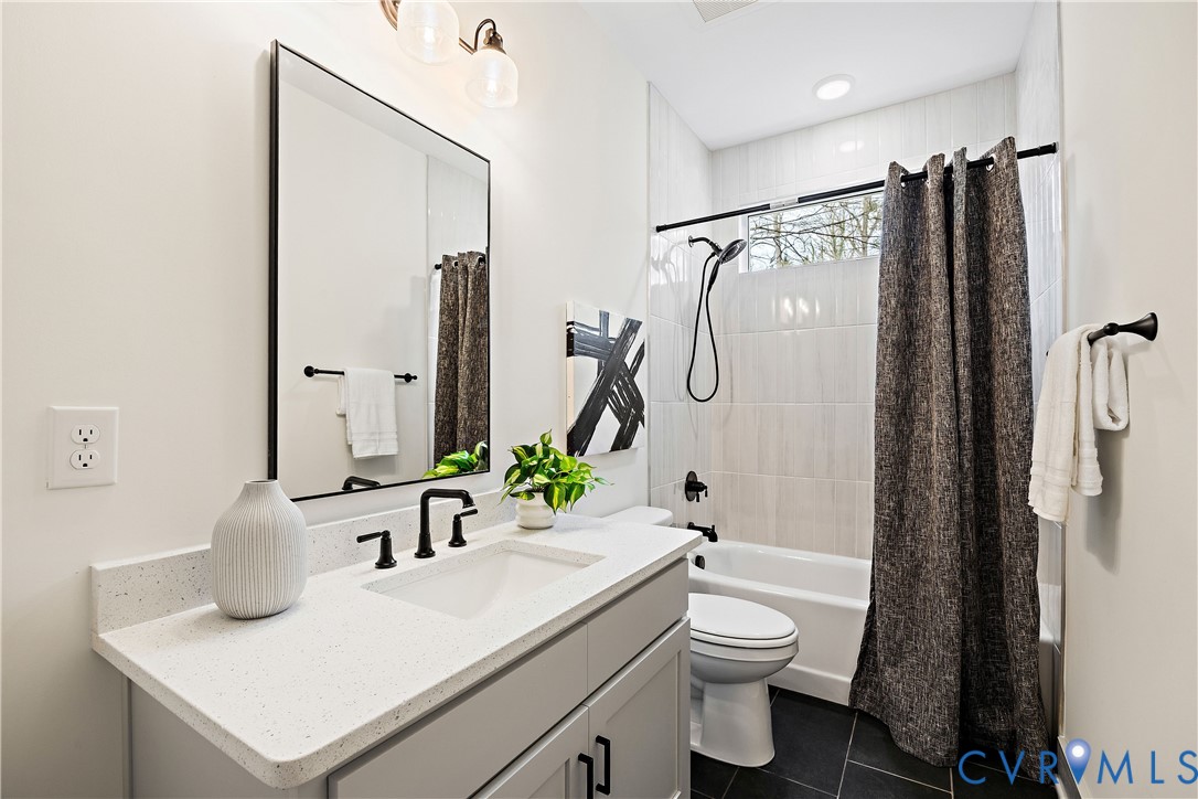1st floor full bathroom. Modern bathroom featuring a single vanity with a quartz-finish countertop and an integrated sink, matte black faucet, and a black-framed rectangular mirror