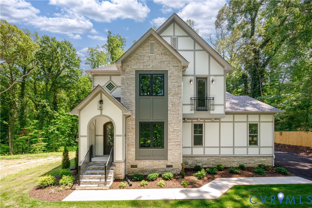 Stone and Tudor-style exterior featuring a covered arched entry, black-framed windows, and a second-story Juliet balcony