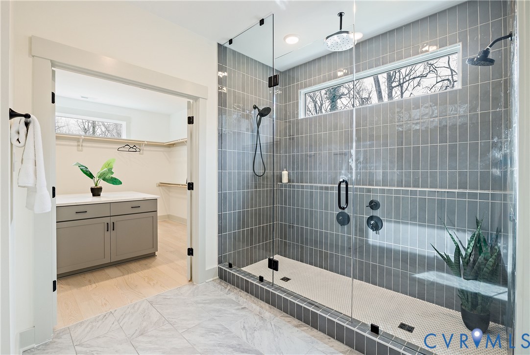 Walk-in shower featuring full glass enclosure, vertical subway tile, dual shower heads, and a linear transom window
