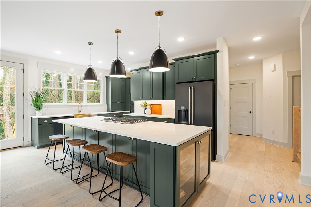 Contemporary kitchen featuring dark green cabinetry, a large central island with seating, a built-in cooktop, and light wood-finish flooring