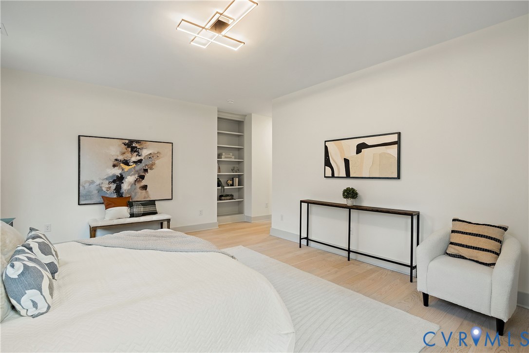 2nd floor primary bedroom featuring light wood-finish flooring, a modern ceiling light fixture, walk-in closet & en-suite bathroom