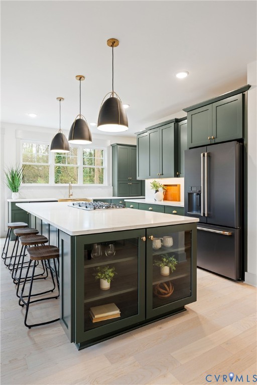 Kitchen featuring dark green cabinetry, a central island with a built-in cooktop, light wood-finish flooring, and black appliances