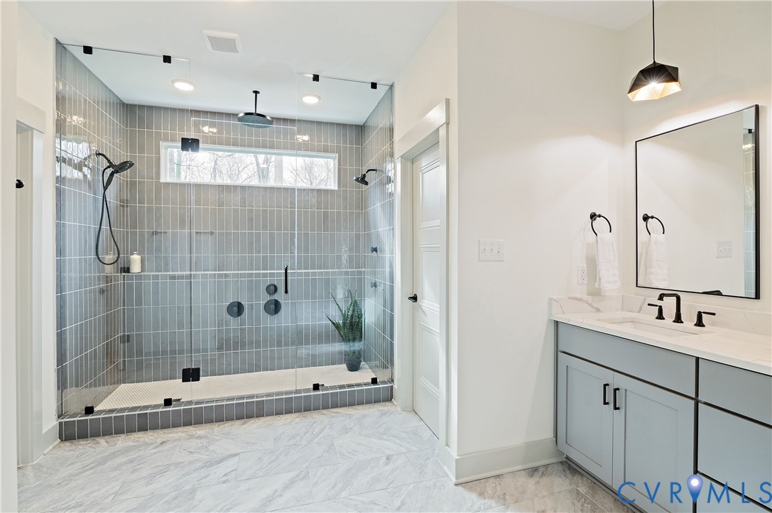 Spacious walk-in shower featuring glass enclosure, vertical subway tile, dual showerheads, and a linear transom window