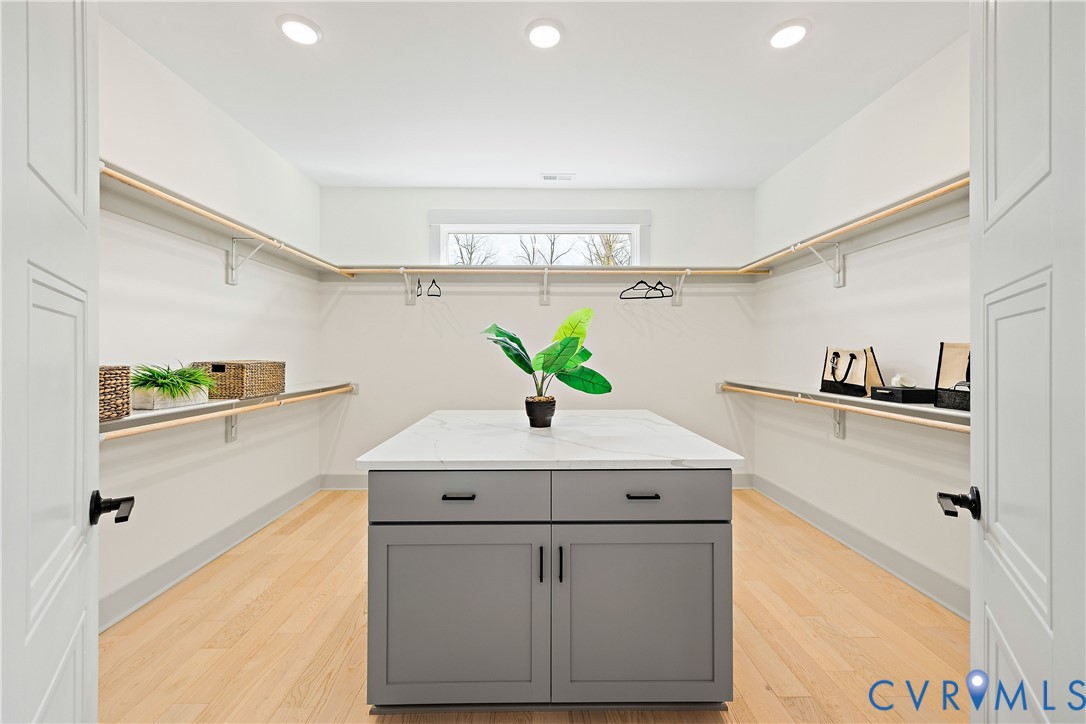 Primary bedroom custom closet featuring light wood-finish flooring, recessed lighting, and an island with quartz