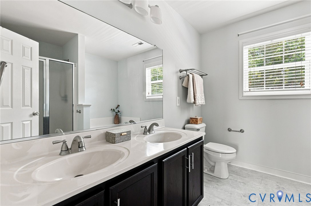 Dual sink vanity with dark wood-finish cabinetry, a large wall-mounted mirror, and sleek chrome fixtures