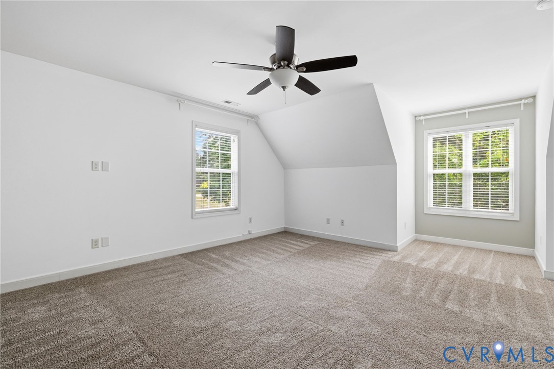 Spacious room featuring vaulted ceilings, a contemporary ceiling fan, and two windows with blinds