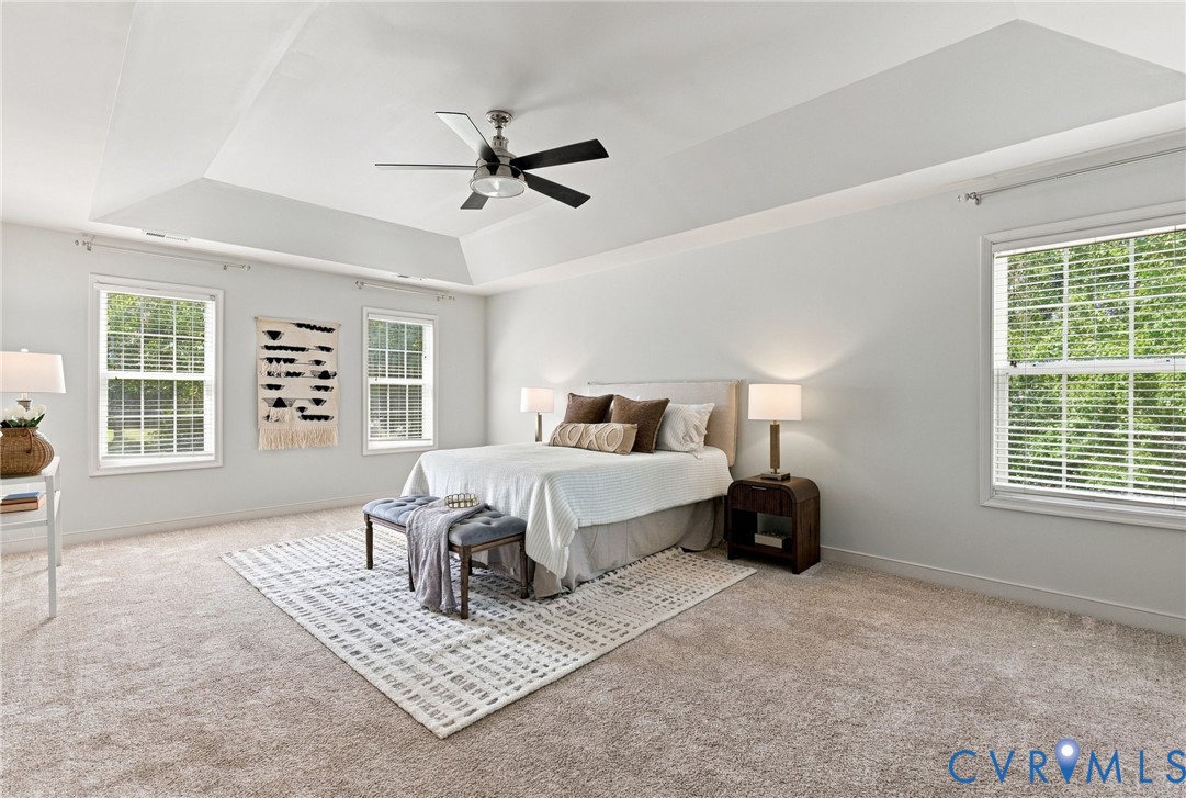 Recessed ceiling with an integrated ceiling fan, multiple double-hung windows, and neutral carpeting