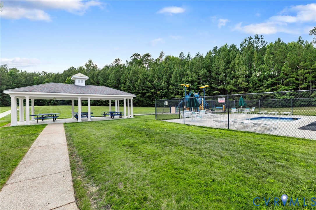 Community amenity area featuring a covered picnic pavilion, swimming pool with surrounding concrete deck, and a fenced recreational water play structure