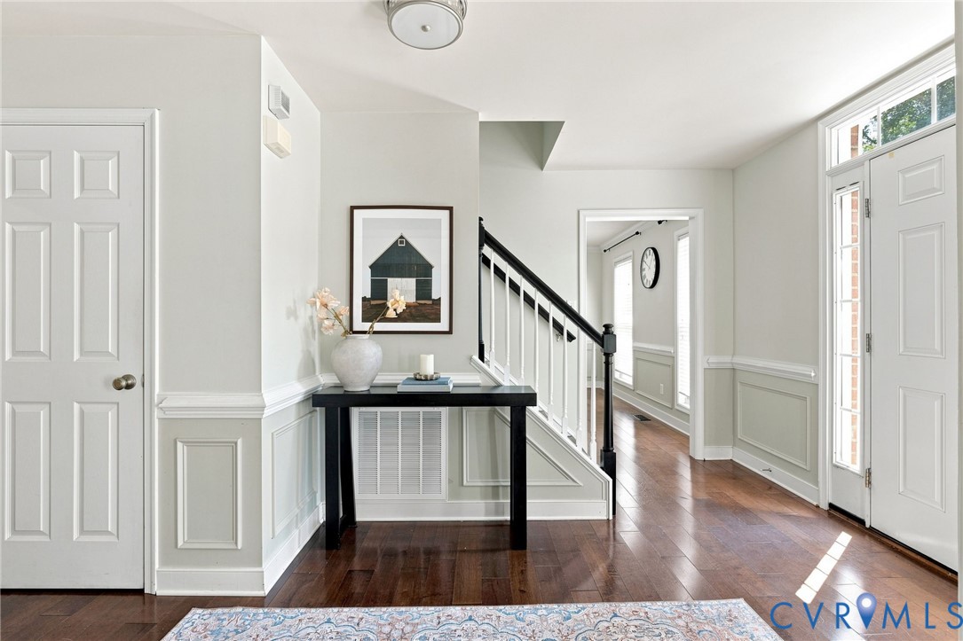 Hardwood-finish flooring, paneled wainscoting, white trim, and a staircase with a black handrail