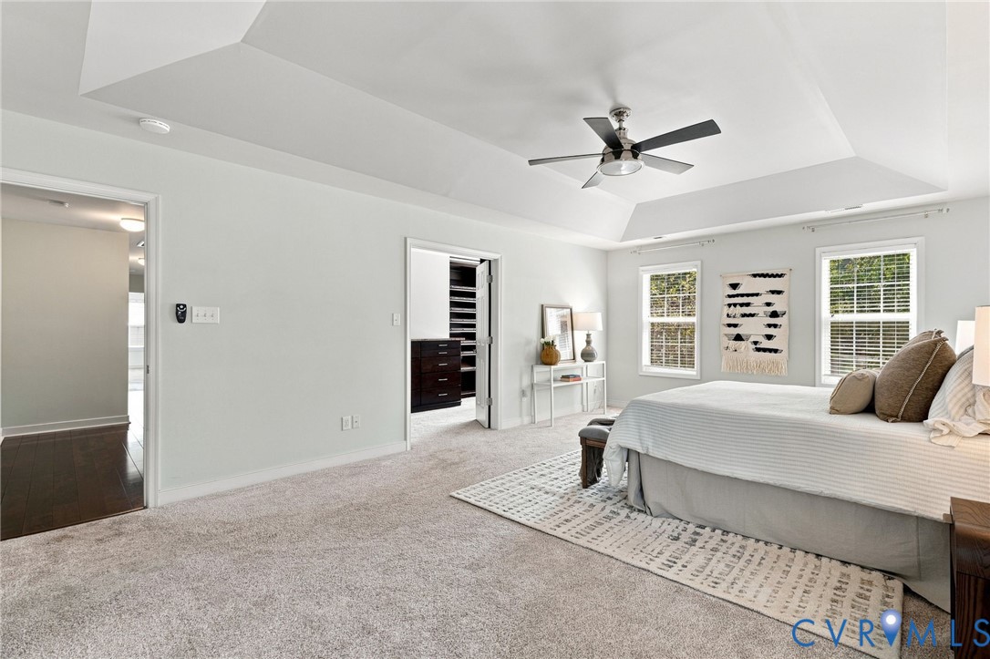 Tray ceiling with a ceiling fan, two windows, and carpeting throughout