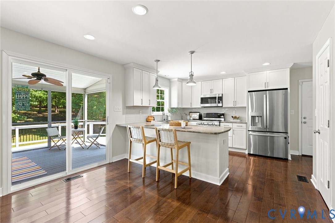 Kitchen featuring wood-finish flooring, white cabinetry, stainless steel appliances, and a central island with counter seating