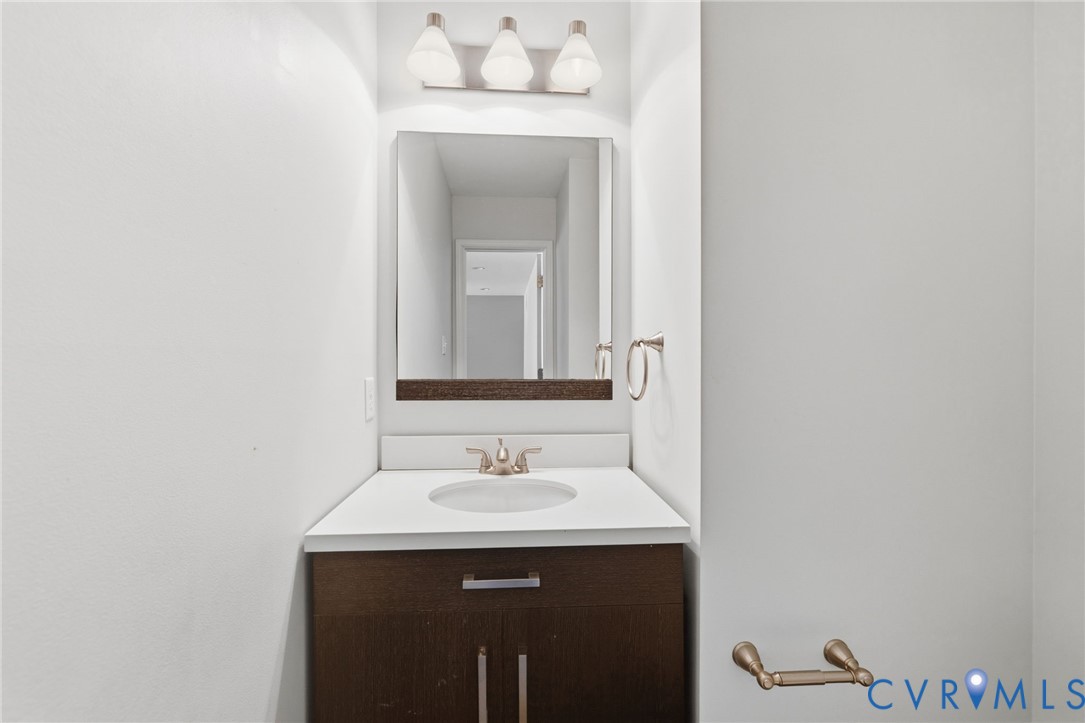 Bathroom vanity featuring a dark wood-finish cabinet, white countertop with an integrated sink, brushed nickel faucet, and a wall-mounted mirror