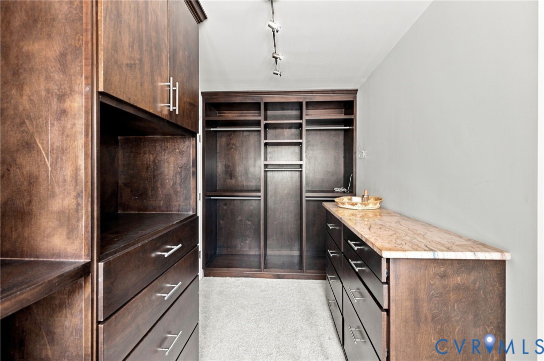 Built-in custom cabinetry with dark wood-finish, extensive shelving, integrated clothing rods, and a light-toned stone countertop