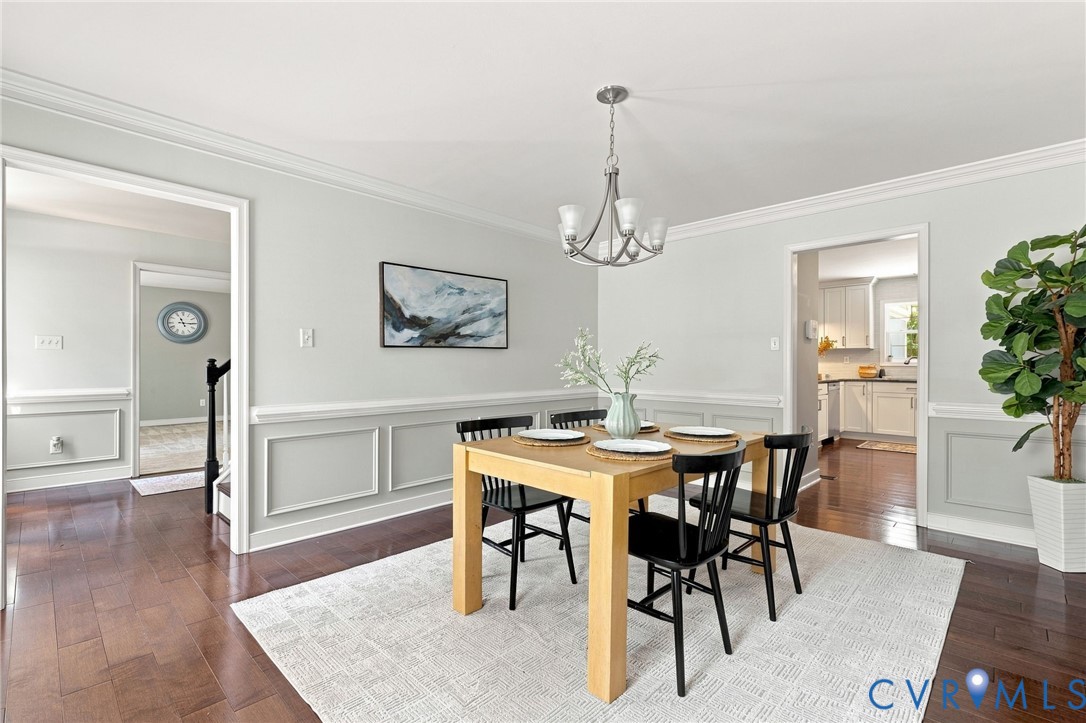Hardwood-finish flooring, crown molding, chair rail with wainscoting, and a ceiling-mounted chandelier