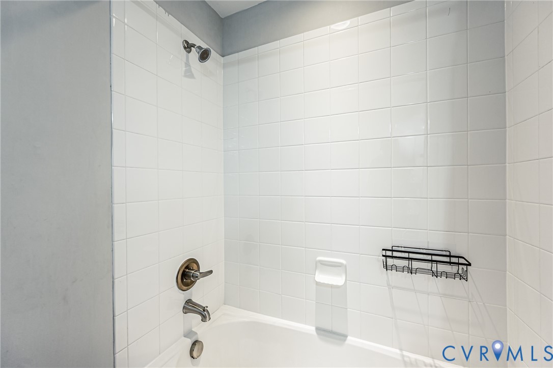 Bathtub shower combination featuring white subway tile surround, bronze-finish fixtures, and a wall-mounted shower head