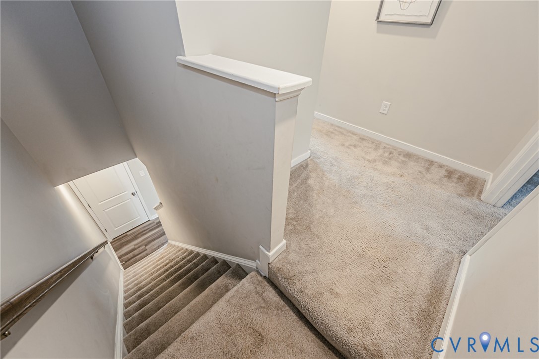 Carpeted staircase and hallway featuring light gray walls, white trim, and a white interior door
