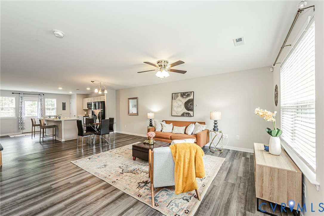 Open-concept living area featuring wood-finish flooring, a ceiling fan, and multiple windows