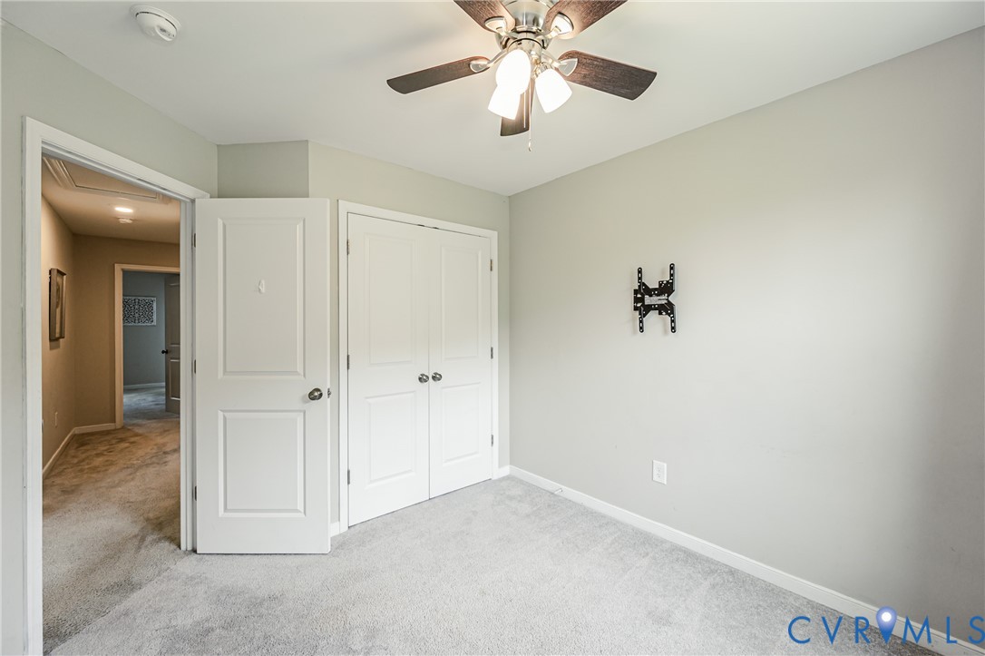 Carpeted room featuring a ceiling fan with integrated lighting, a double-door closet, and a wall-mounted television bracket