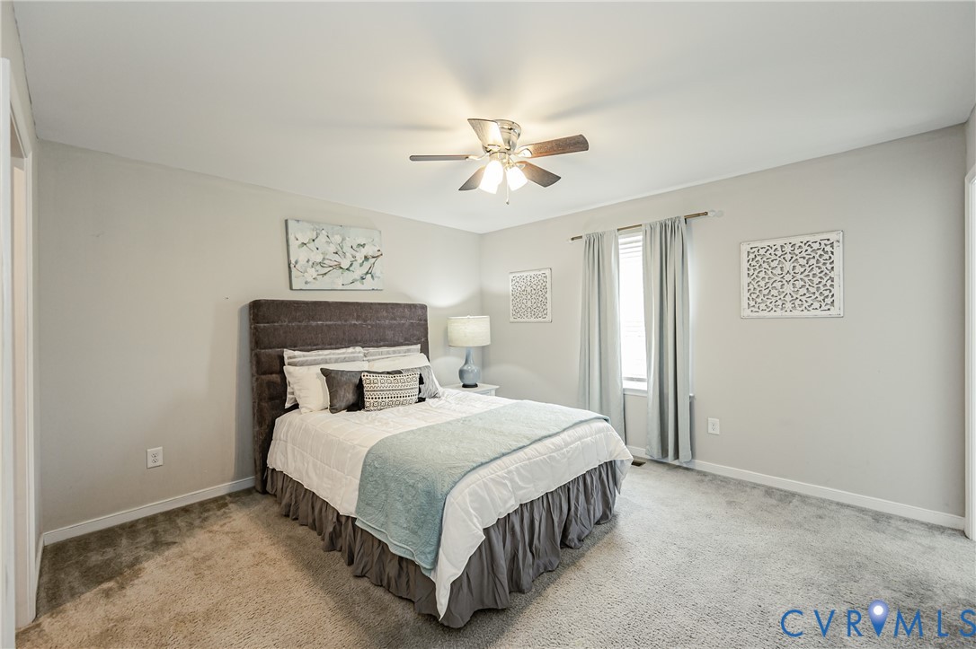 Carpeted interior room featuring light-toned walls, a single window with curtain rods, and a ceiling fan with integrated lighting