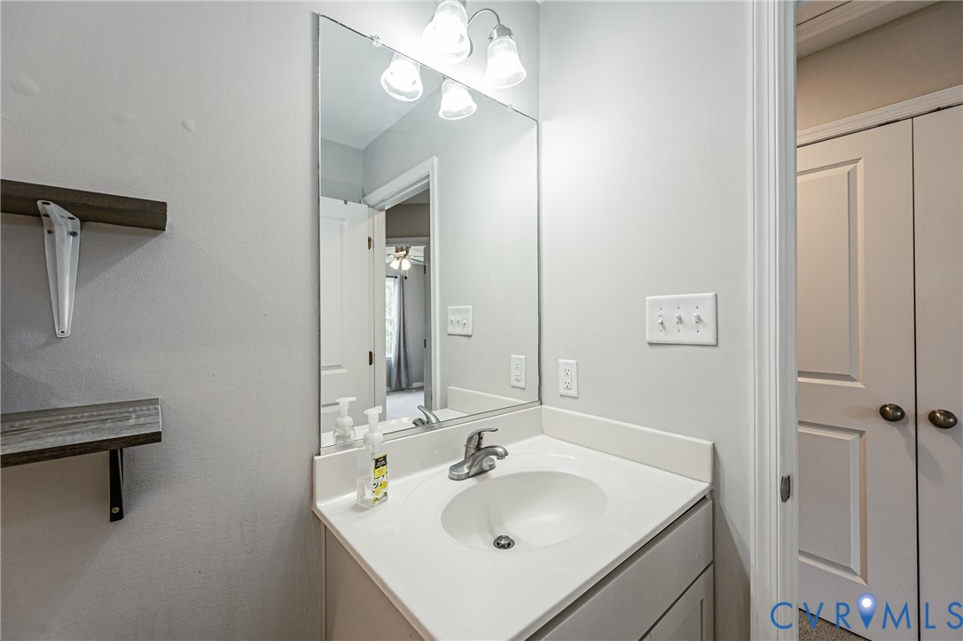 Bathroom vanity with an integrated sink, polished chrome faucet, and overhead three-bulb light fixture