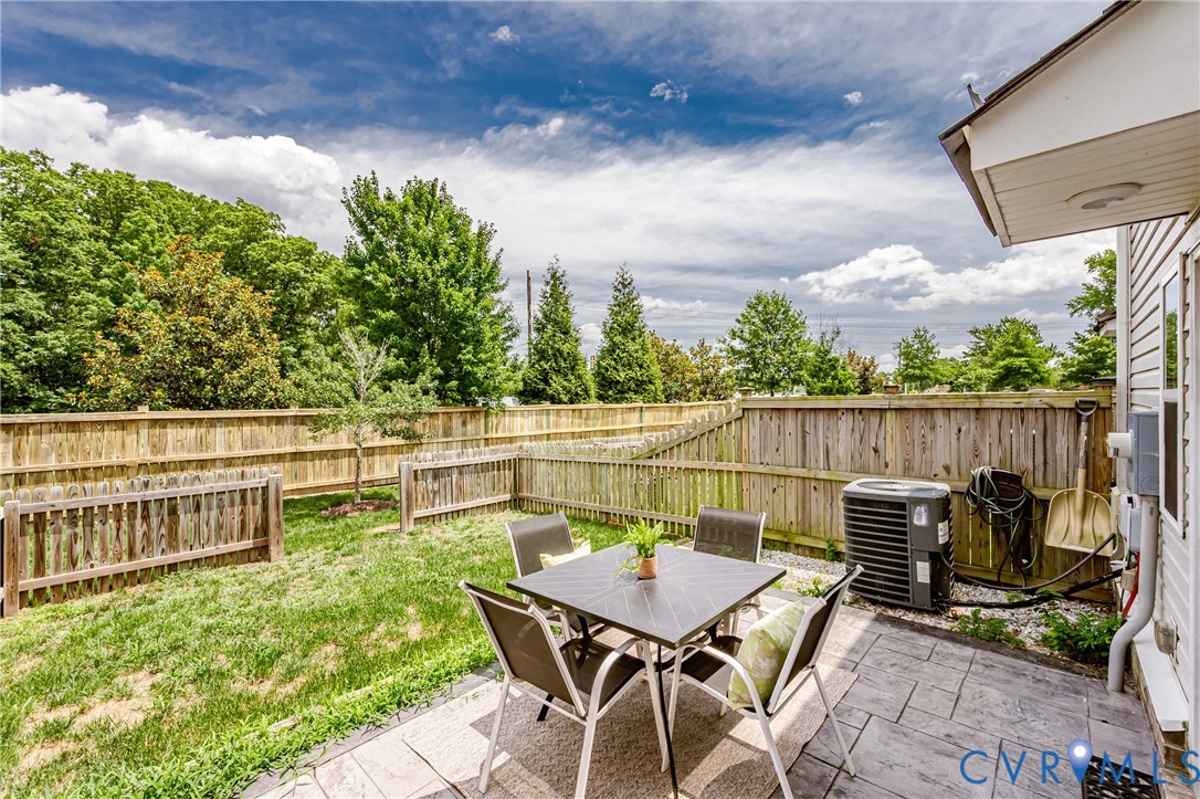 Fenced backyard featuring a textured stamped concrete patio, a manicured lawn, and mature perimeter trees
