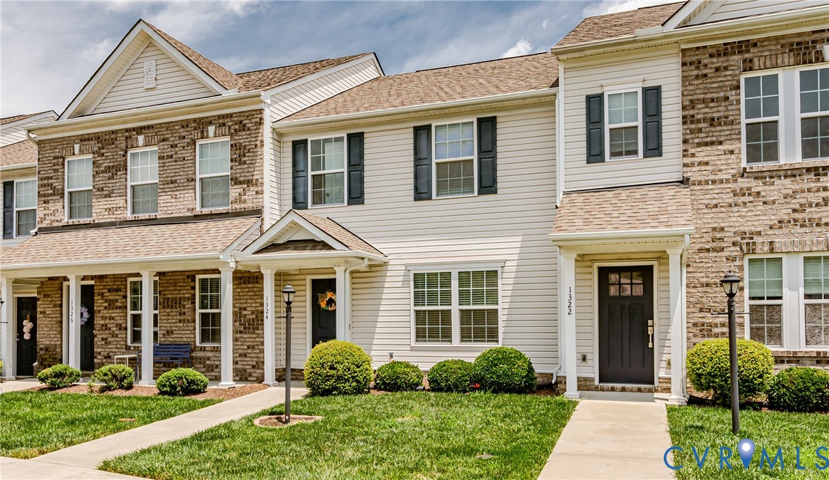 Townhome exterior featuring light-colored siding, dark window shutters, a covered entry, and a dark front door with glass panels