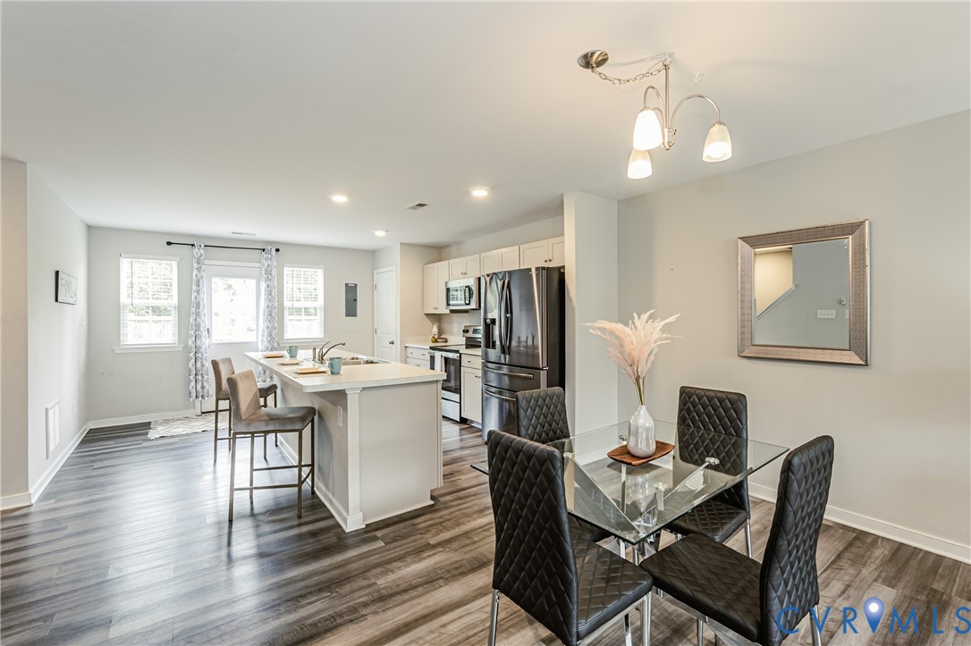 Open-concept living area featuring wood-finish flooring, a kitchen island with seating, white cabinetry, and stainless steel appliances