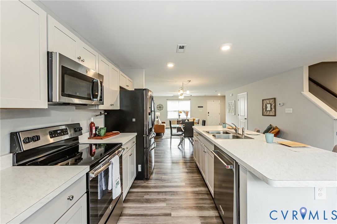 Open-concept kitchen featuring an island with dual sinks, stainless steel appliances, white cabinetry, wood-finish flooring, and recessed lighting