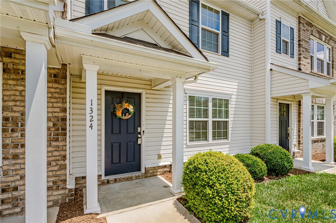 Inviting front entrance featuring a dark paneled door, white columns, brick facade accents, and horizontal siding