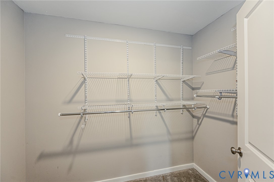 Walk-in closet featuring wire shelving, multiple hanging rods, light-toned walls, white trim, and a neutral carpet