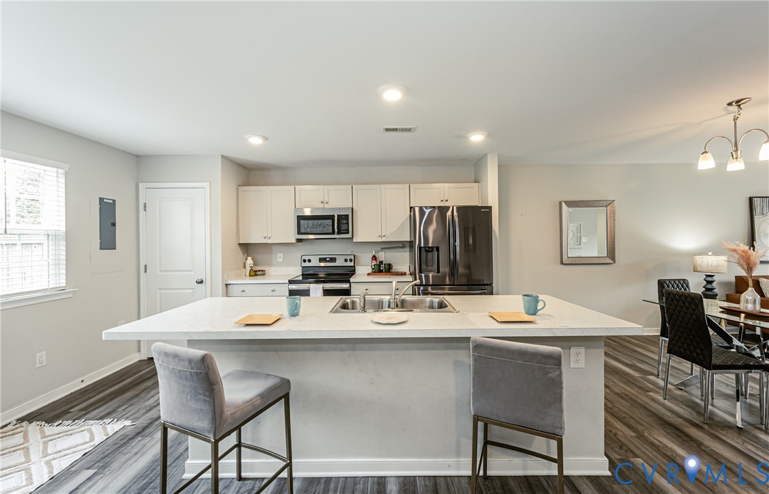 Open-concept kitchen featuring an expansive island with seating, a double basin sink, and stainless steel appliances