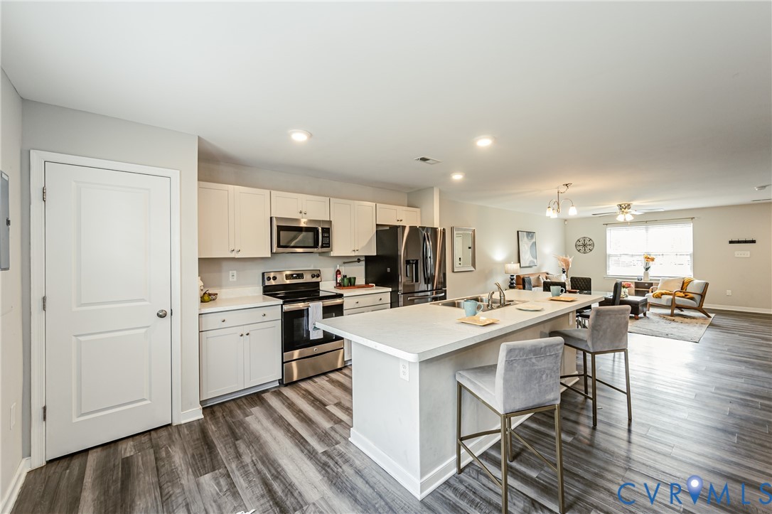Open-concept kitchen featuring white cabinetry, stainless steel appliances, and wood-finish flooring