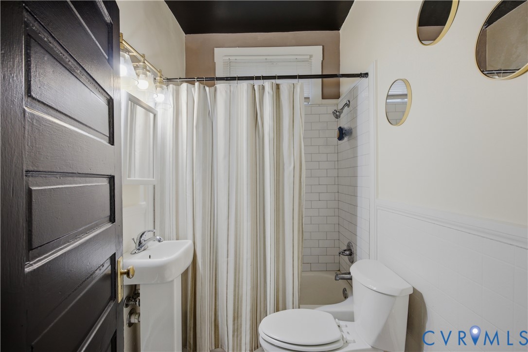 Bathroom with a pedestal sink, white subway tile shower surround, and a paneled lower wall